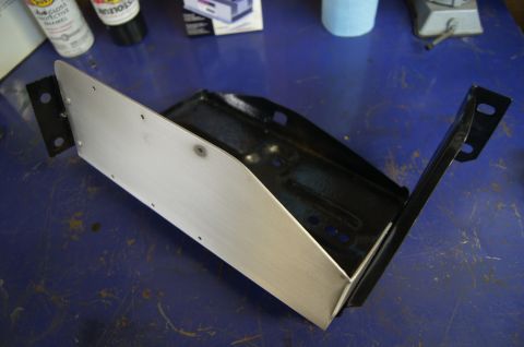 1979 Ford Bronco - A metal bracket assembly is shown on a workbench, with spray cans and other items in the background.