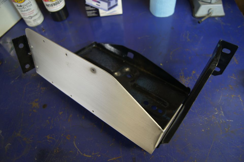 Metal bracket with brushed aluminum and black steel components on a blue workbench