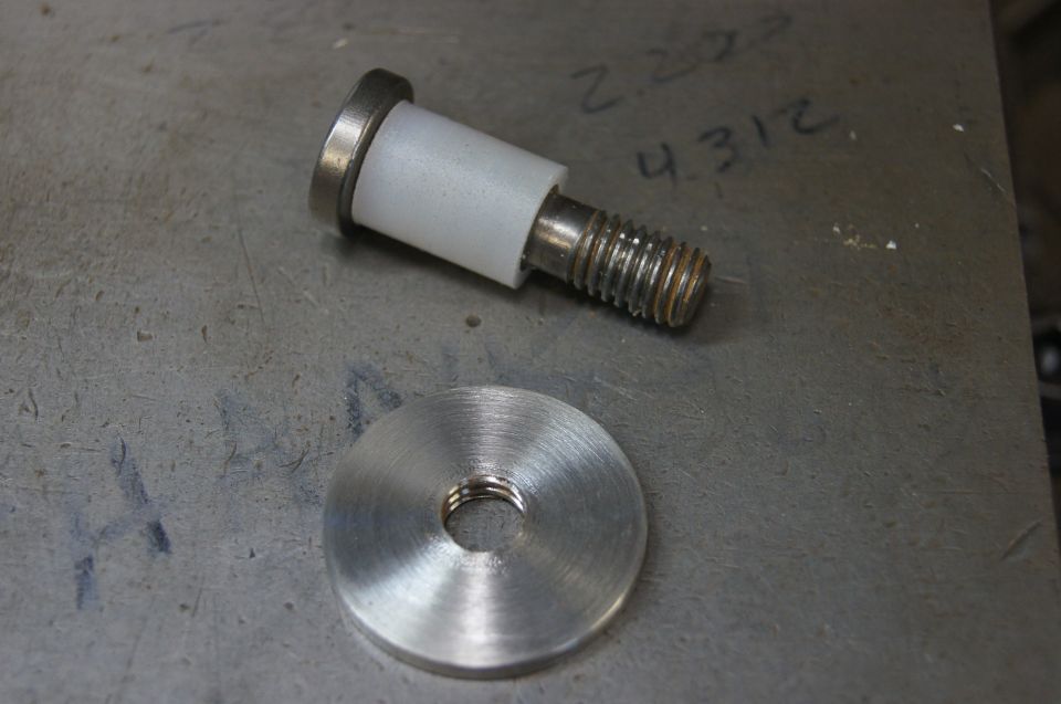 Metal bolt with white plastic spacer and threaded washer on a metal surface