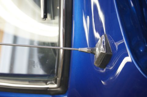 1979 Ford Bronco - The base of a car antenna is visible on the bright blue body panel next to the window.