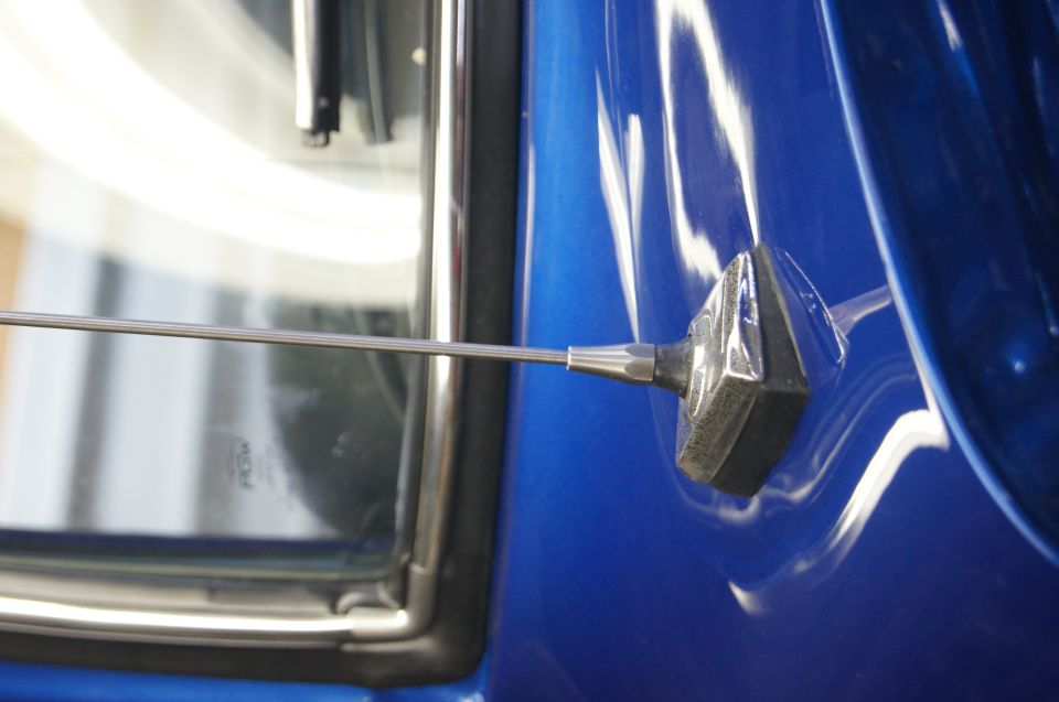 Close-up of a chrome antenna base on a blue car door, with a window visible to the left