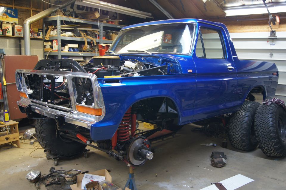 Blue 1979 Ford Bronco in a garage, hood up, front end disassembled, large tires