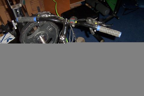 1980 Ford Bronco - Handlebars of a bicycle with rubber grips, brake levers and a small cycle-computer reading 2034, with barbell weight plates and clutter beh…