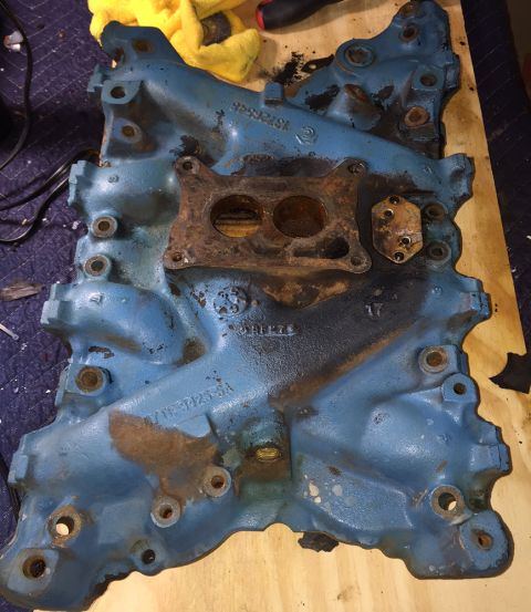 1978 Ford Bronco - This blue engine intake manifold shows signs of wear and rust, with a carburetor mounting plate attached.