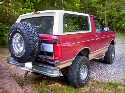 1995 Ford Bronco - Rear view of a red Ford Bronco with a tan stripe and a white removable top.