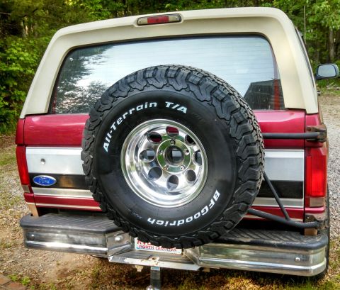 1995 Ford Bronco - Rear view of a red and tan Ford Bronco, showing its spare tire and chrome bumper.
