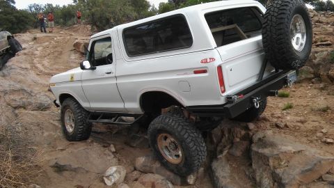 1979 Ford Bronco - White Ford Bronco tackling a challenging rocky off-road course with a spare tire mounted at the rear.