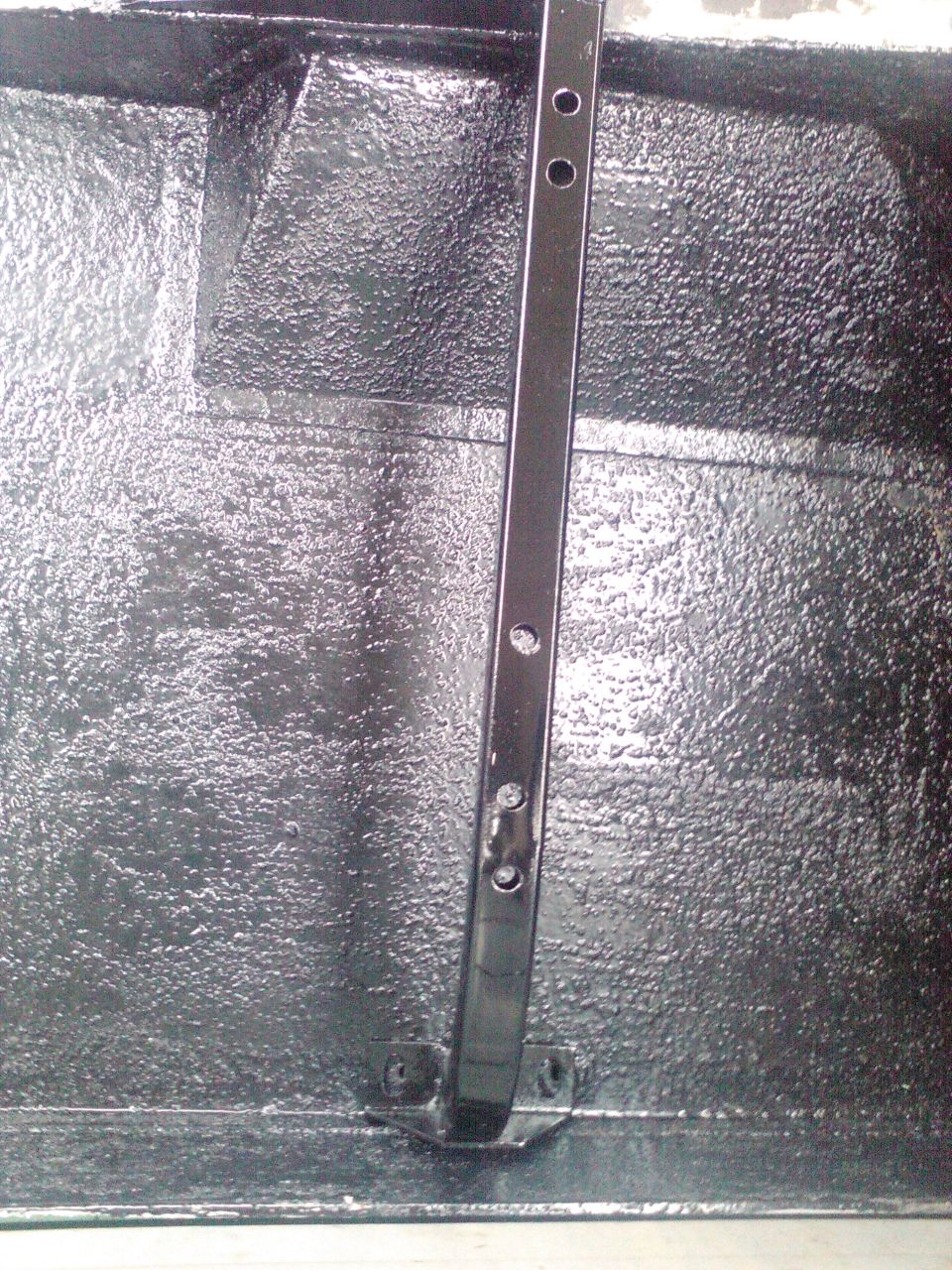 Close-up of the textured black interior of a truck bed with a metal support bracket attached