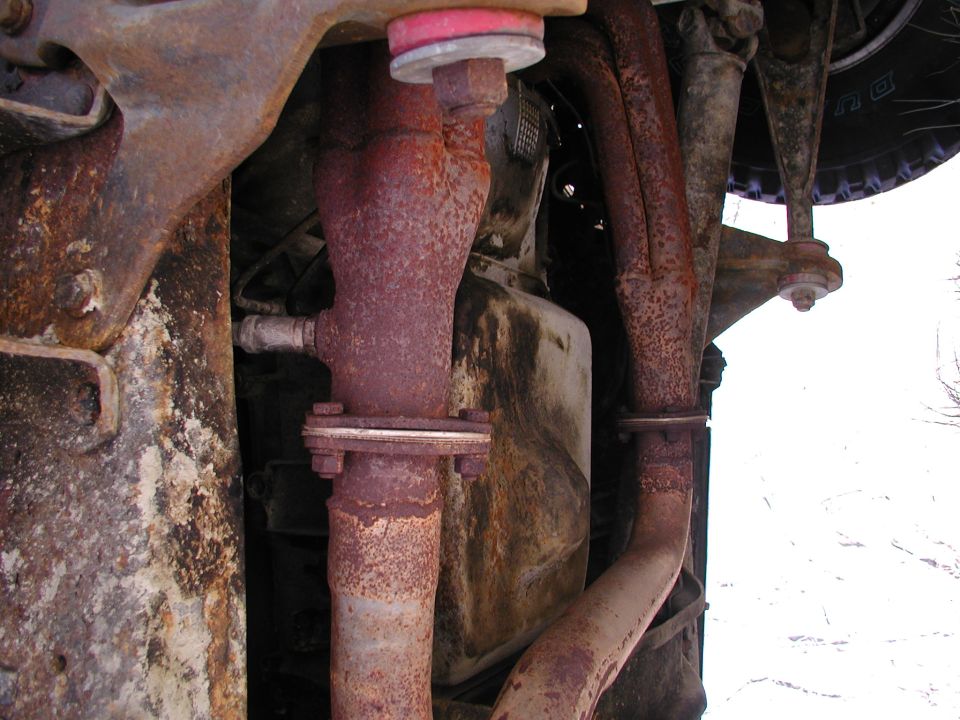 Close-up of rusted exhaust pipes and catalytic converter from underneath a vehicle