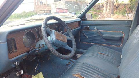1980 Ford Fairmont - The interior of an older car shows worn blue seats and a dashboard with wood-grain accents.