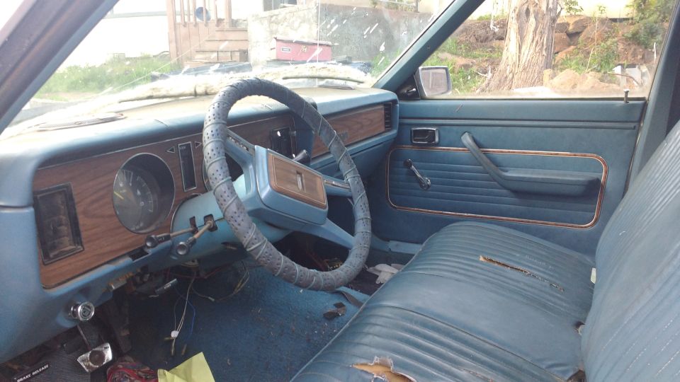 Interior of a car with blue seats and wood-grain dashboard trim. Steering wheel has a cover