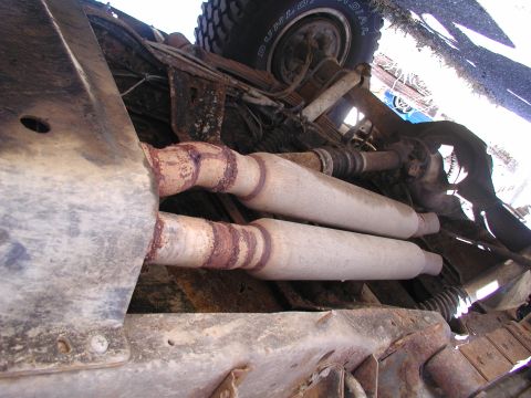 1990 Ford Bronco - The underside of a vehicle reveals its dual exhaust system and a portion of a tire.