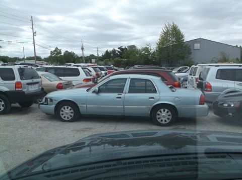 1999 Mercury Grand Marquis - A light blue sedan is parked in a lot full of vehicles under a cloudy sky.