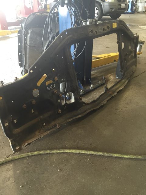 1978 Ford Bronco - A disassembled vehicle frame part is shown in a workshop, with a hose on the floor and another vehicle in the background.