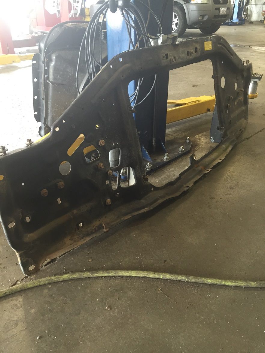 Black metal vehicle frame section with mounting holes and rust, on a workshop floor