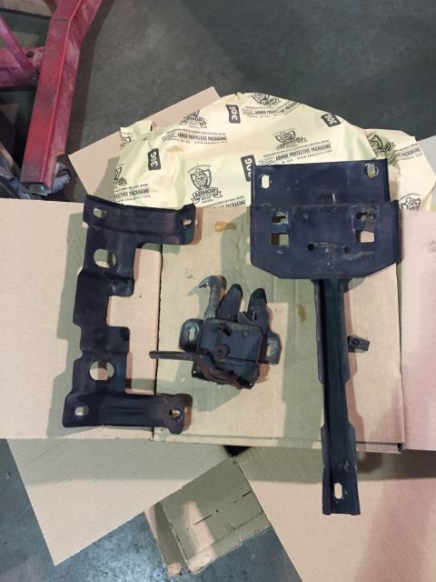 1978 Ford Bronco - Car parts including hood latch and brackets are laid out on cardboard.