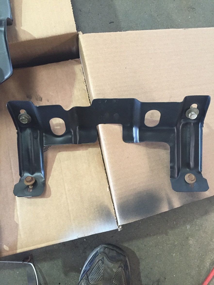 Black metal bracket with bolts, resting on cardboard