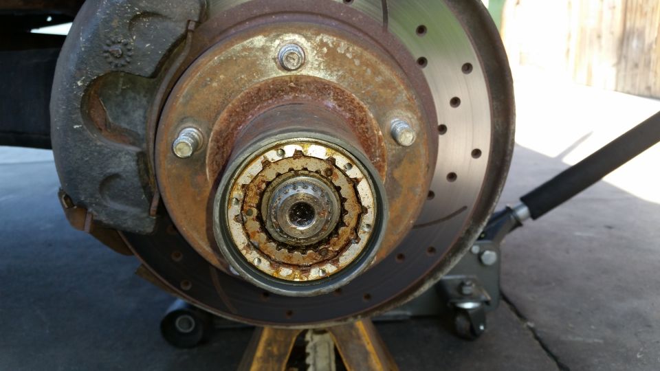 Close-up of a rusty front wheel hub assembly with a brake rotor and caliper