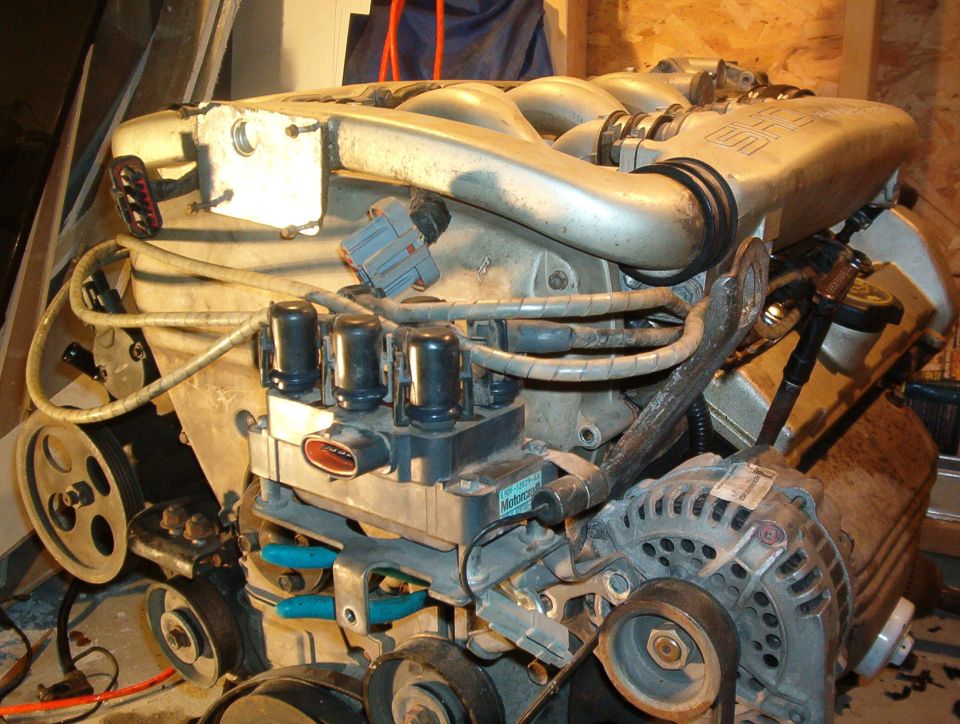 Ford V6 engine on a stand with aluminum intake, coil packs and alternator visible