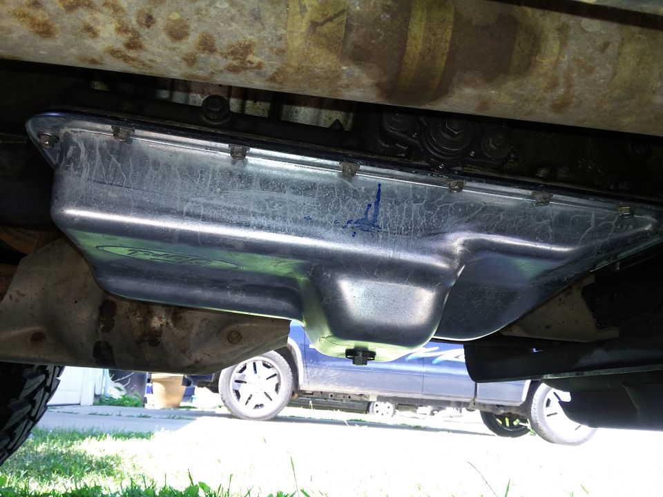 Underside view of an oil pan and transmission. Another vehicle is visible in the background