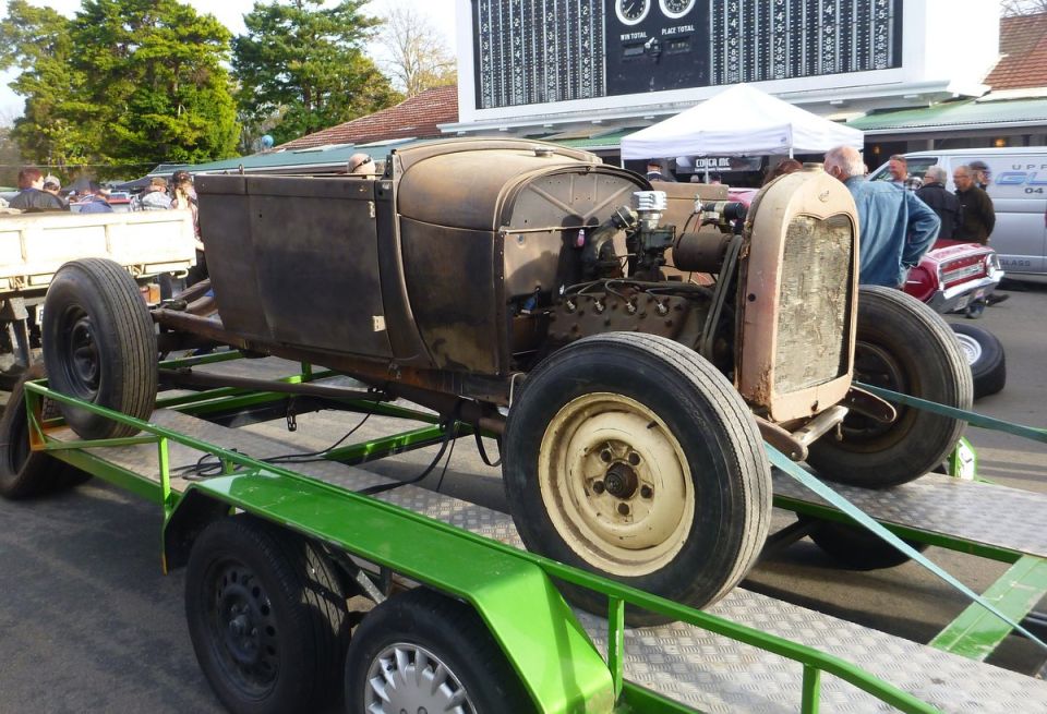 Rusty hot rod body and engine on a green trailer, being towed