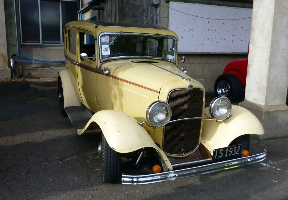 Yellow vintage sedan with a brown stripe, chrome bumper, and license plate 'TS 1932'
