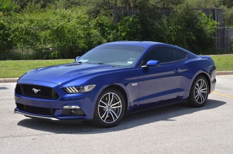 2015 Ford Mustang - A blue 2015 Ford Mustang coupe is parked outdoors with trees in the background.