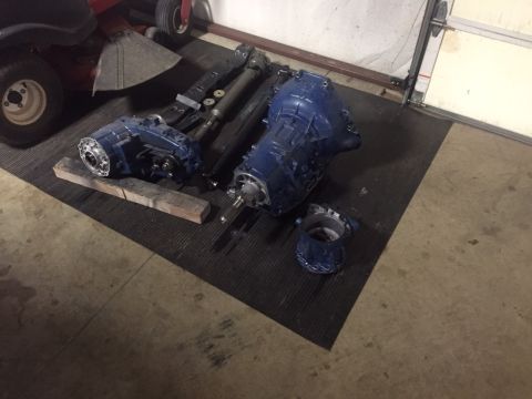 1982 Ford Bronco - Vehicle drivetrain components, including transmissions and a transfer case, are laid out on a mat in a garage.