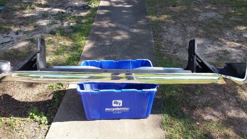 1976 Ford Ranchero - Rear bumper assembly with mounting brackets, placed on blue recycling bins outdoors.