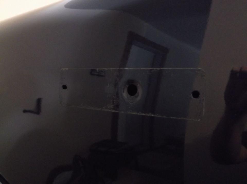 Close-up of a dark vehicle body panel showing two mounting holes and a central larger hole, possibly for a license plate bracket
