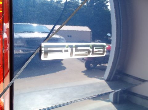 2005 Ford F-150 - The F-150 emblem is visible on the side of a blue truck, with reflections of other vehicles and buildings in the shiny paint.