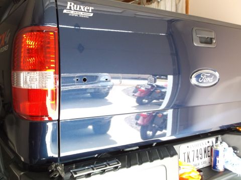 2005 Ford F-150 - Dark blue Ford F-150 tailgate with a Ford emblem and a Ruxer sticker. Reflections show motorcycles.