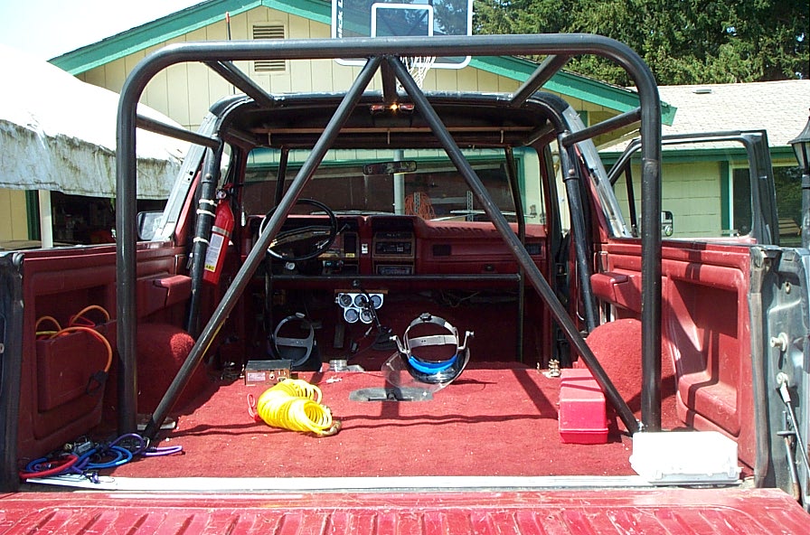 Rear view into dark red Bronco cargo area with black roll cage, red carpet, seats removed, tools inside