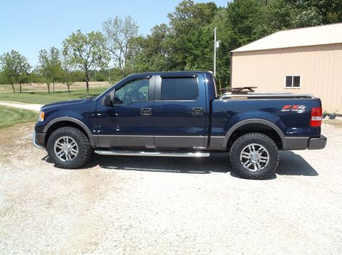 2005 Ford F-150 - This dark blue Ford F-150 pickup truck is seen from the side, parked on a gravel lot.