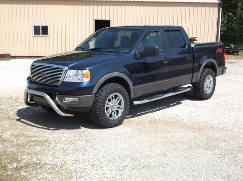 2005 Ford F-150 - This blue Ford F-150 pickup truck is parked outside a building on a gravel lot.
