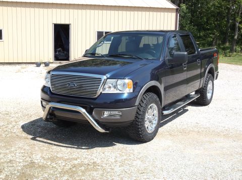 2005 Ford F-150 - This blue 2005 Ford F-150 pickup truck is equipped with a chrome bull bar and aftermarket wheels, parked in front of a light-colored buildi…