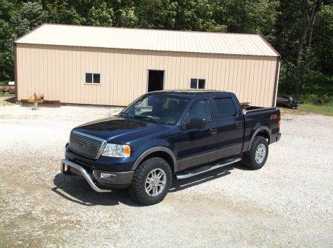 2005 Ford F-150 - Dark blue Ford F-150 pickup truck parked in front of a tan metal building with trees in the background.