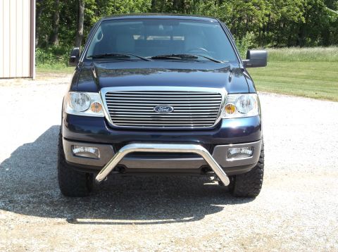 2005 Ford F-150 - A dark blue Ford F-150 pickup truck is parked outside on a gravel driveway with trees in the background.
