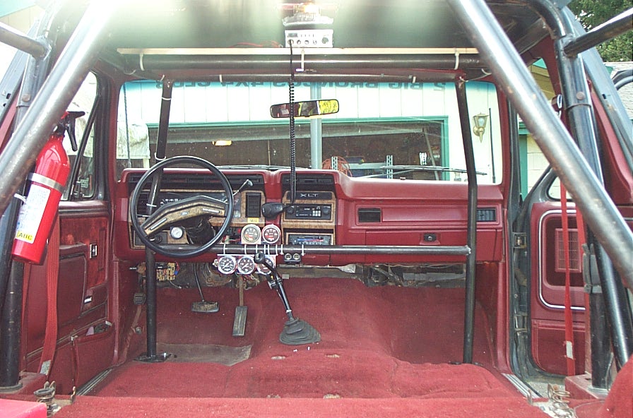 Gutted red Ford Bronco interior with roll cage, aftermarket gauges, floor shifter and fire extinguisher