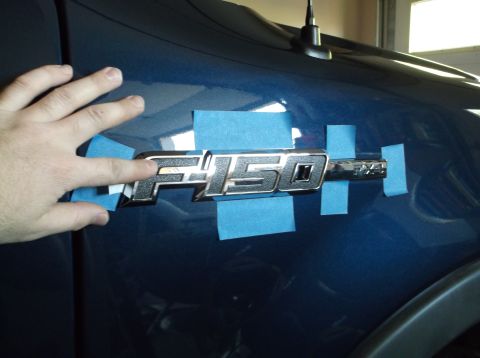 2005 Ford F-150 - A hand is shown taping an F-150 badge on a blue vehicle.