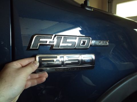 2005 Ford F-150 - A hand holds a chrome Ford F-150 FX4 emblem over the factory installed emblem on a blue truck.