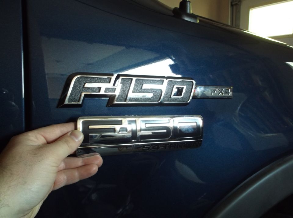 Blue Ford F-150 FX4 emblem held over factory emblem