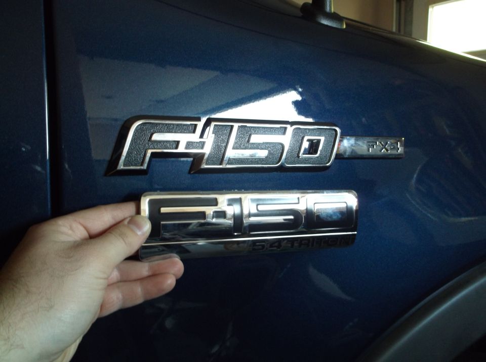Hand holding a Ford F-150 emblem over the F-150 FX4 emblem already on a blue truck