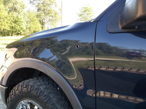 2005 Ford F-150 - This is a side view of a dark blue pickup truck fender, showing some damage and a tire.