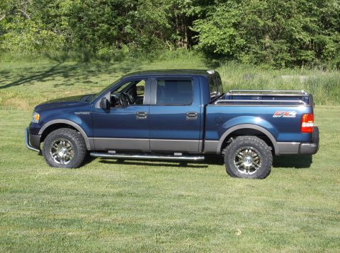 2005 Ford F-150 - A blue Ford F-150 pickup truck is parked on a grassy lawn with trees in the background.