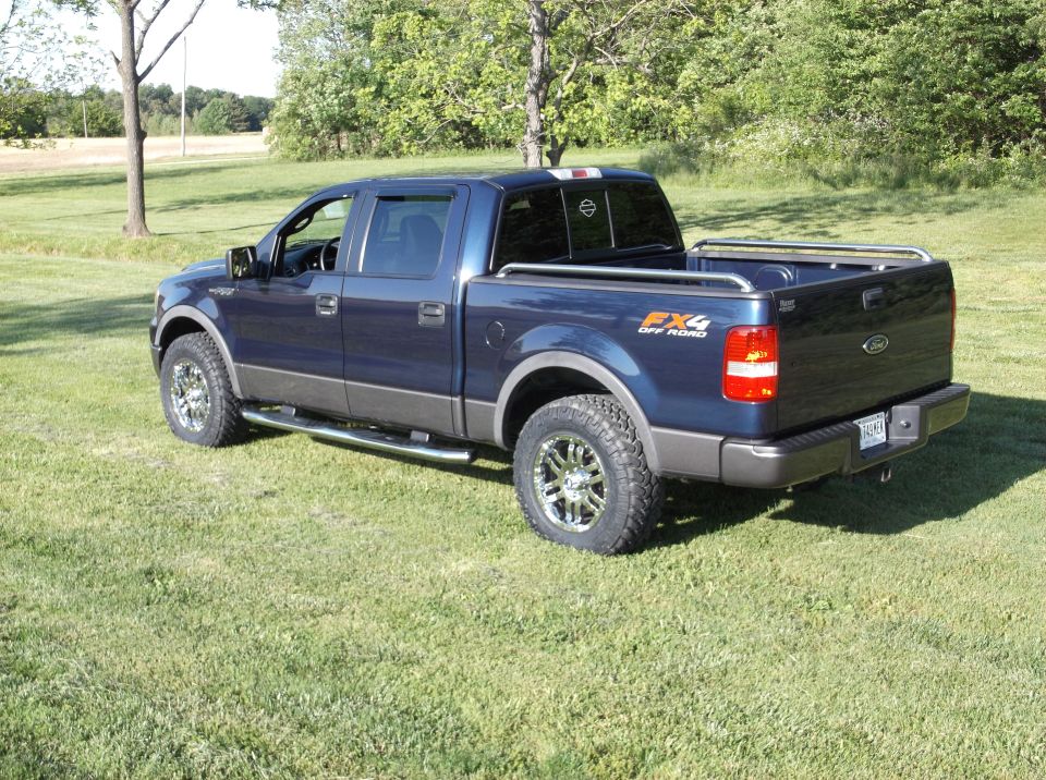 Blue Ford F-150 pickup truck with FX4 Off Road decal on the side, parked on grass with trees in the background