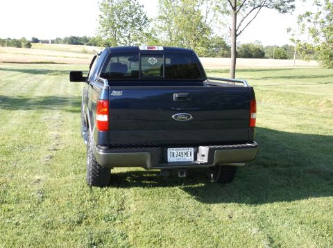 2005 Ford F-150 - Dark blue Ford F-150 pickup truck parked on a grassy field with trees in the background.