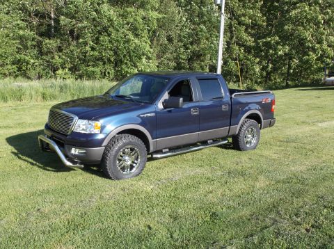 2005 Ford F-150 - Blue 2005 Ford F-150 pickup truck with aftermarket chrome accessories and off-road tires is parked on a grassy lawn.