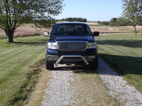 2005 Ford F-150 - A dark blue Ford F-150 pickup truck is parked on a gravel driveway in a rural setting.
