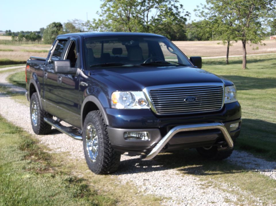 Dark blue Ford F-150 pickup truck with chrome grille and bull bar, parked on a gravel driveway